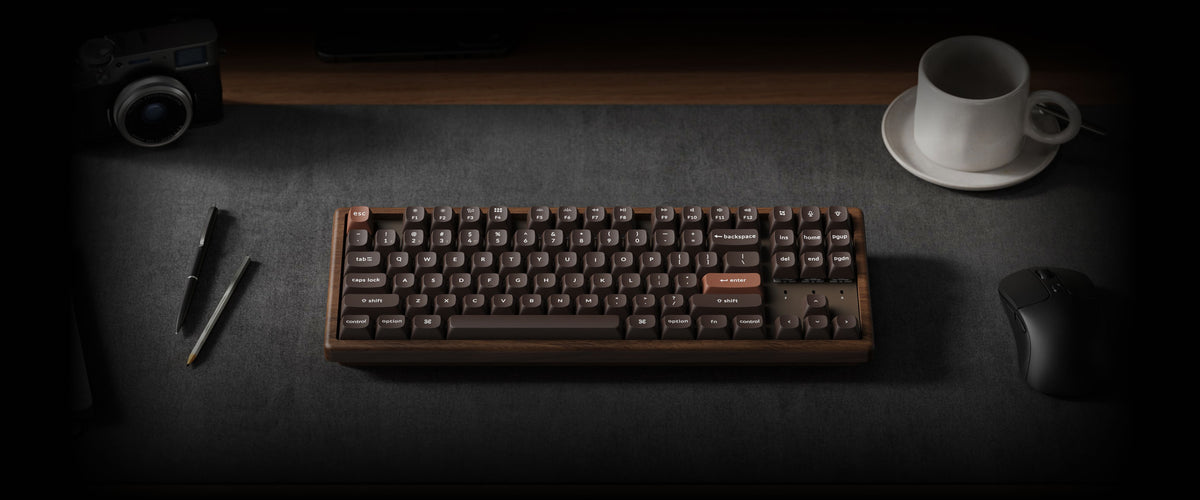 K8 HE All-Wood Edition keyboard on a dark desk with a mouse, camera, coffee cup, and writing tools.